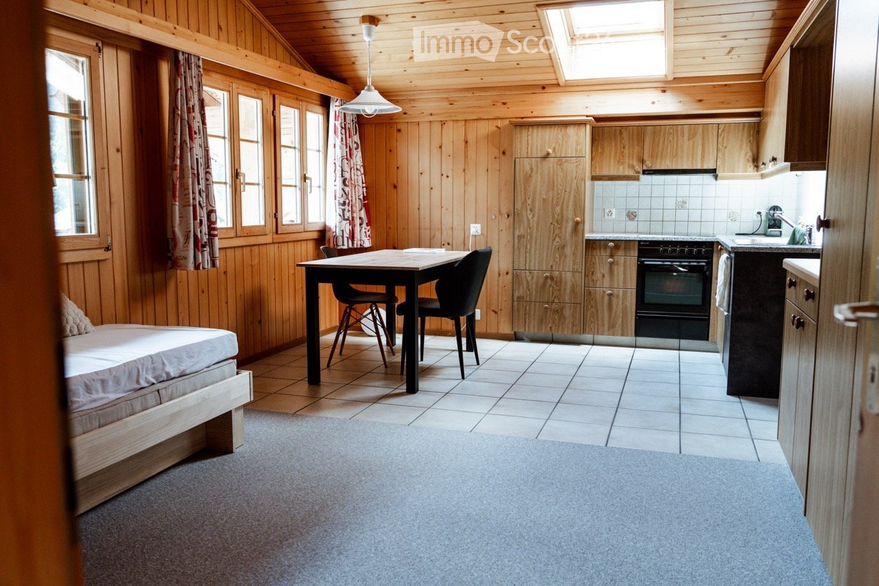 A cozy, wooden-paneled room with a bed, a dining table with chairs, and a kitchen area featuring cabinets, an oven, and a sink.
