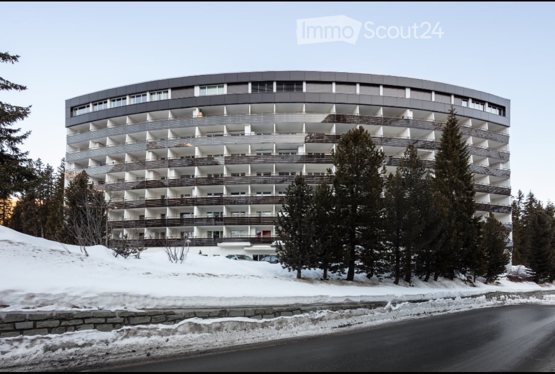 A modern architectural building with many windows and balconies on a snowy hill.