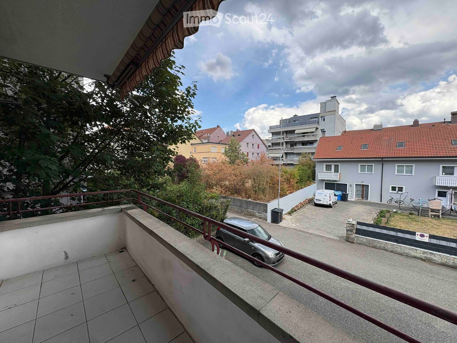 Balcony overlooking a residential area with parked cars, greenery, and neighboring buildings.