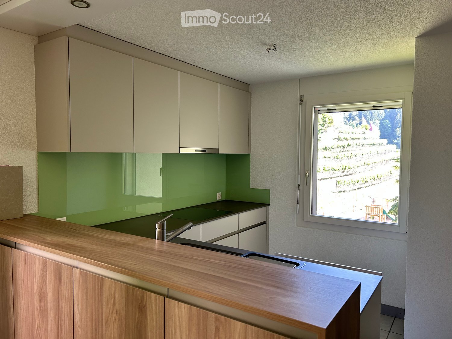 Modern kitchen with light-colored cabinets, green backsplash, wooden countertop, and stainless steel sink.