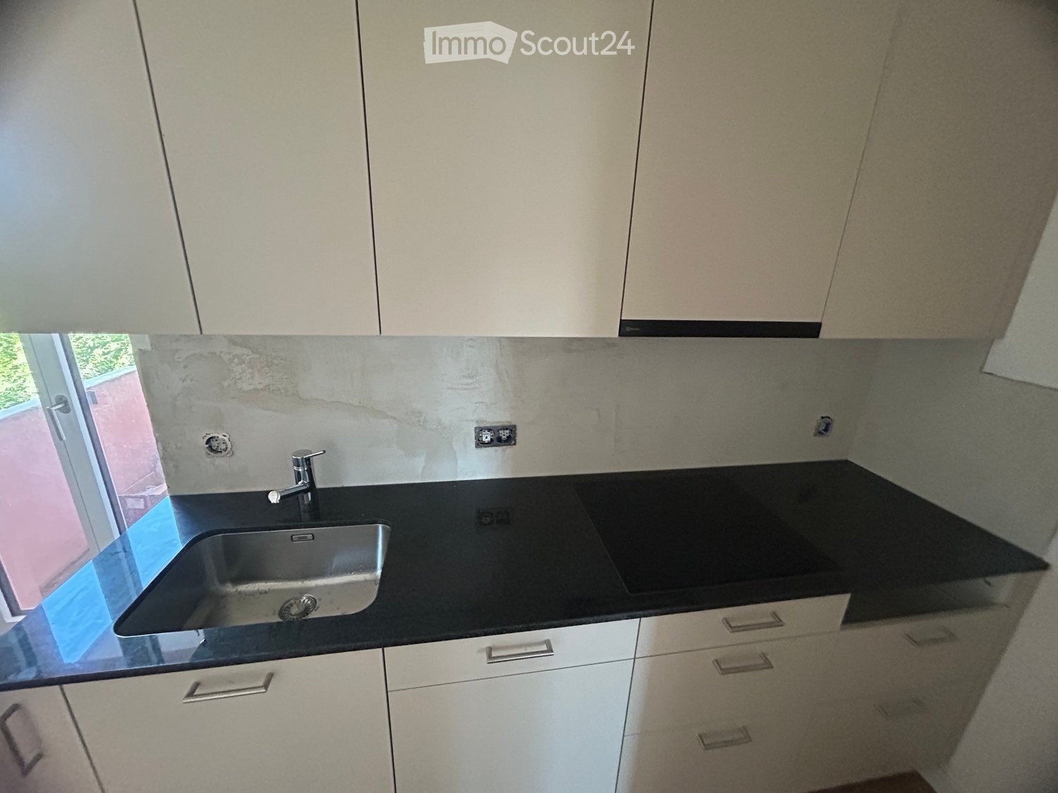 Modern kitchen with white cabinets, black countertop, stainless steel sink, and a faucet.
