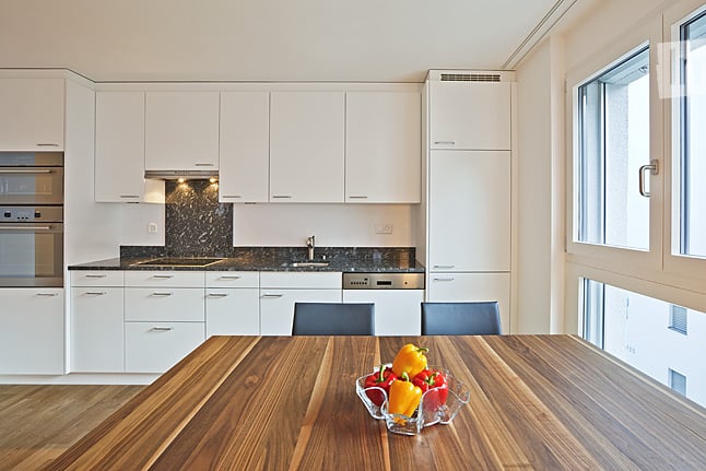 Modern kitchen with white cabinets, stainless steel appliances, granite countertops, and a wooden dining table with chairs.