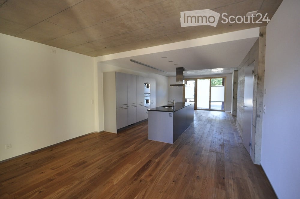 Modern, unfurnished kitchen with light grey cabinets, a central island, and wooden flooring. The space features a sleek design with a large window offering natural light.
