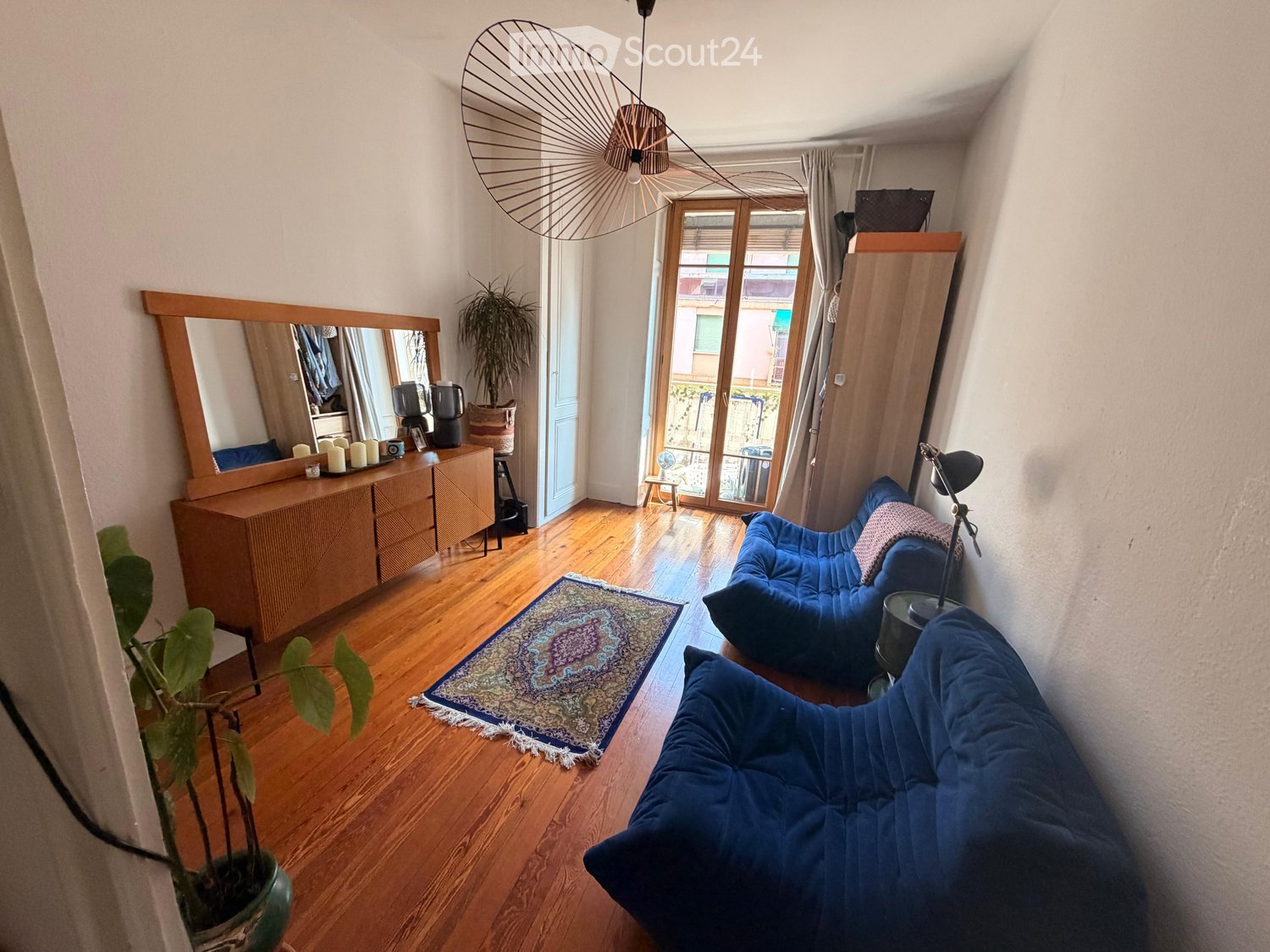 A cozy living room with wooden flooring, a large mirror, a blue sofa, a coffee table, and a decorative rug.