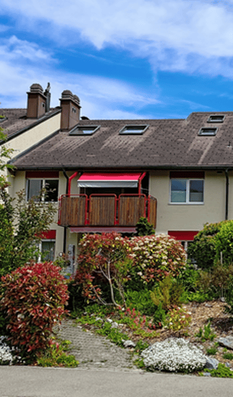 Two-story house with a balcony, red awning, and well-maintained garden.