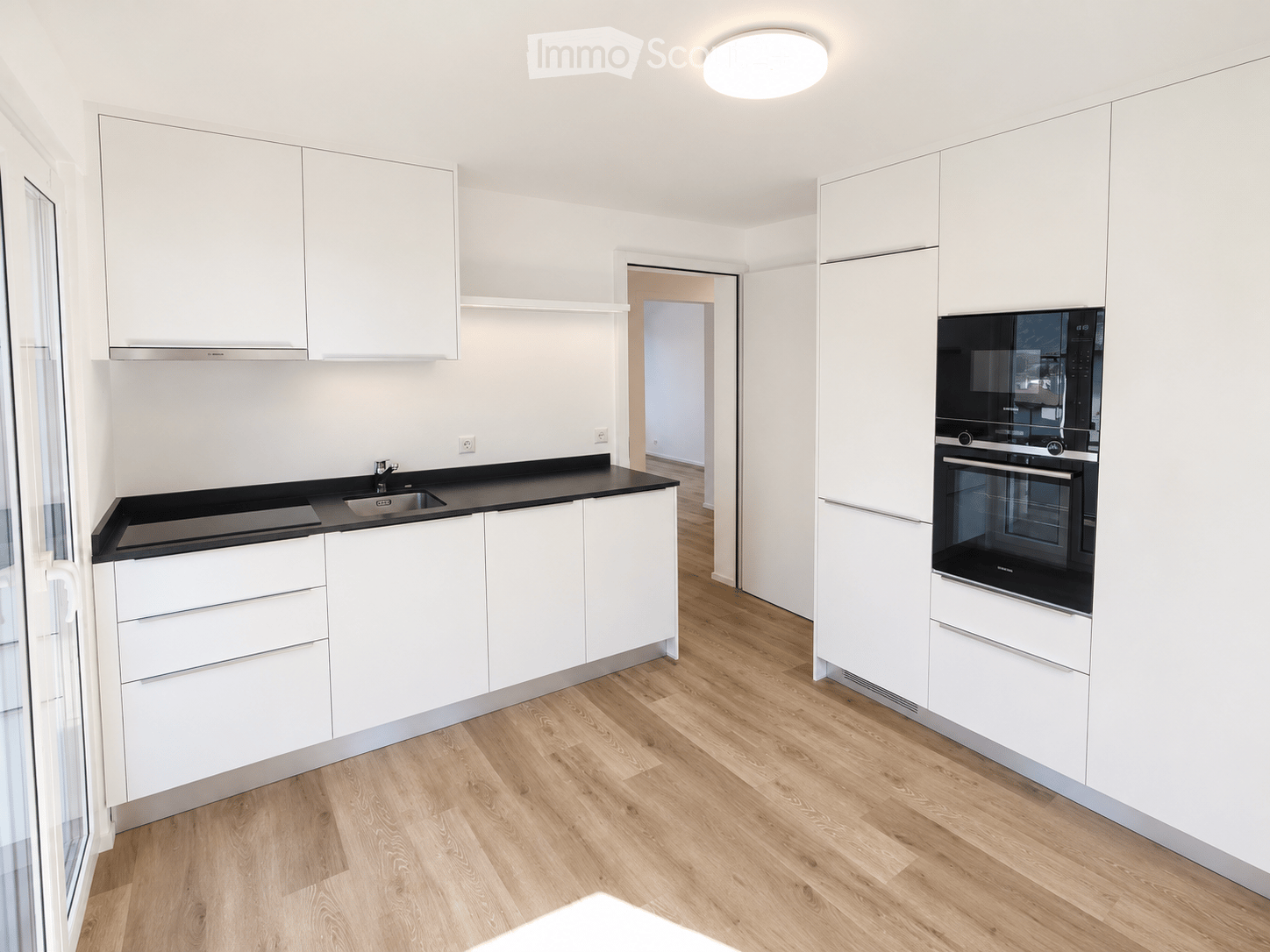 Modern kitchen with white cabinets, black countertop, wooden flooring, and built-in appliances including an oven and microwave.