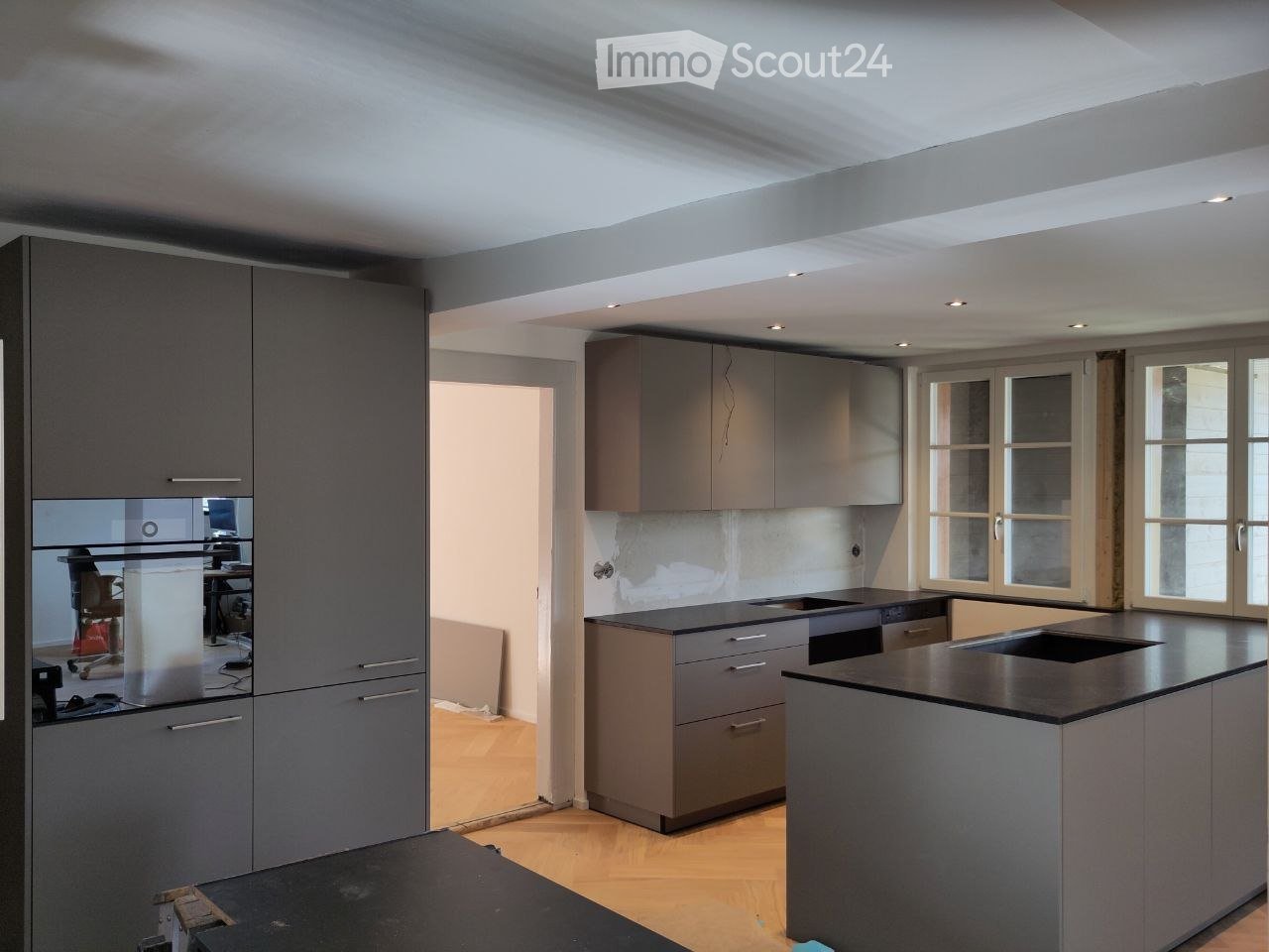 modern kitchen with gray cabinets, black countertops, double sink, oven, wooden floor