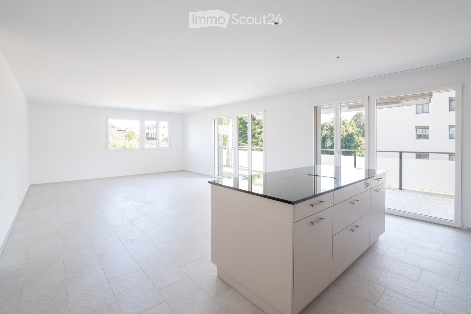 Bright, minimalist kitchen with white tiled flooring, white walls, and a central kitchen island with a black countertop and integrated drawers.