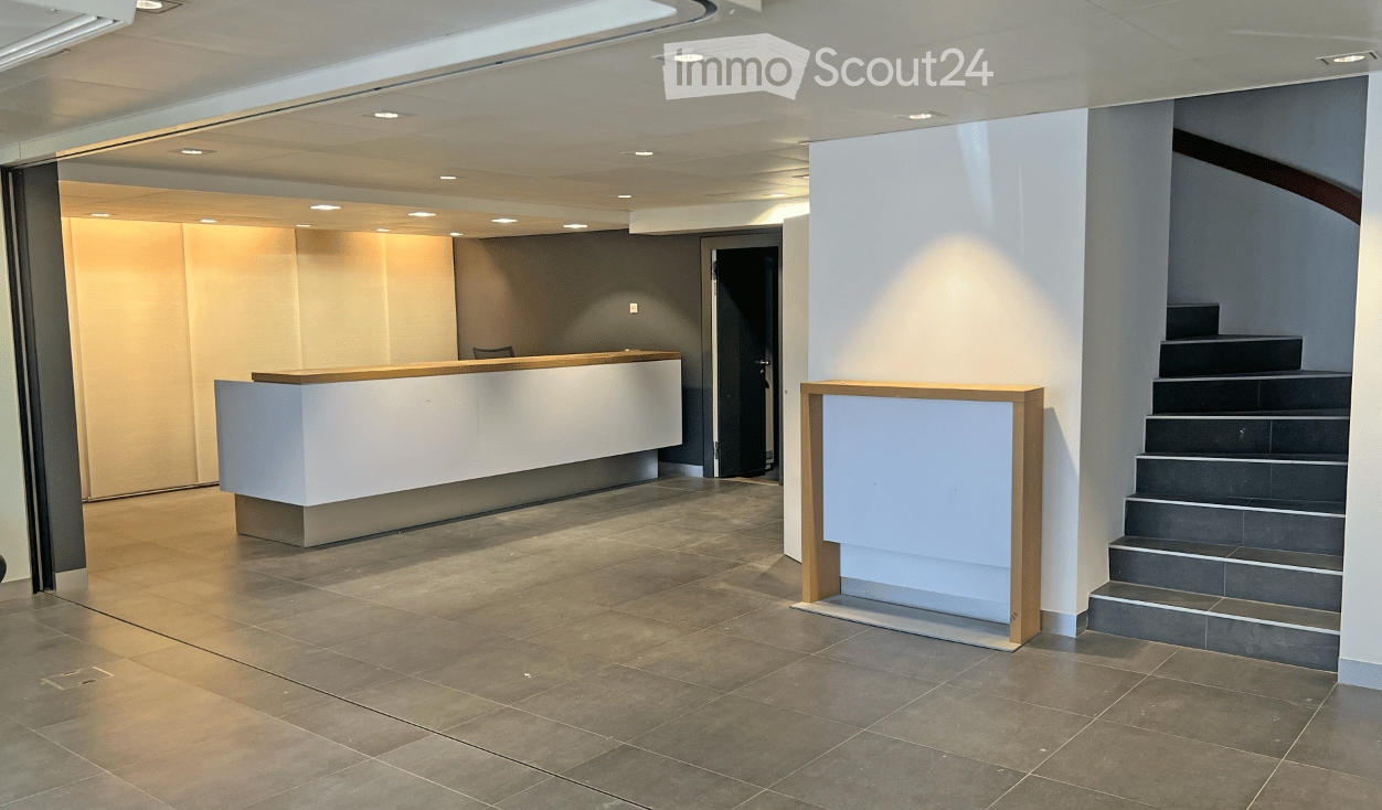 Modern hallway with a reception desk, staircase, and tiled floor. The area features recessed lighting and a sleek, contemporary design.