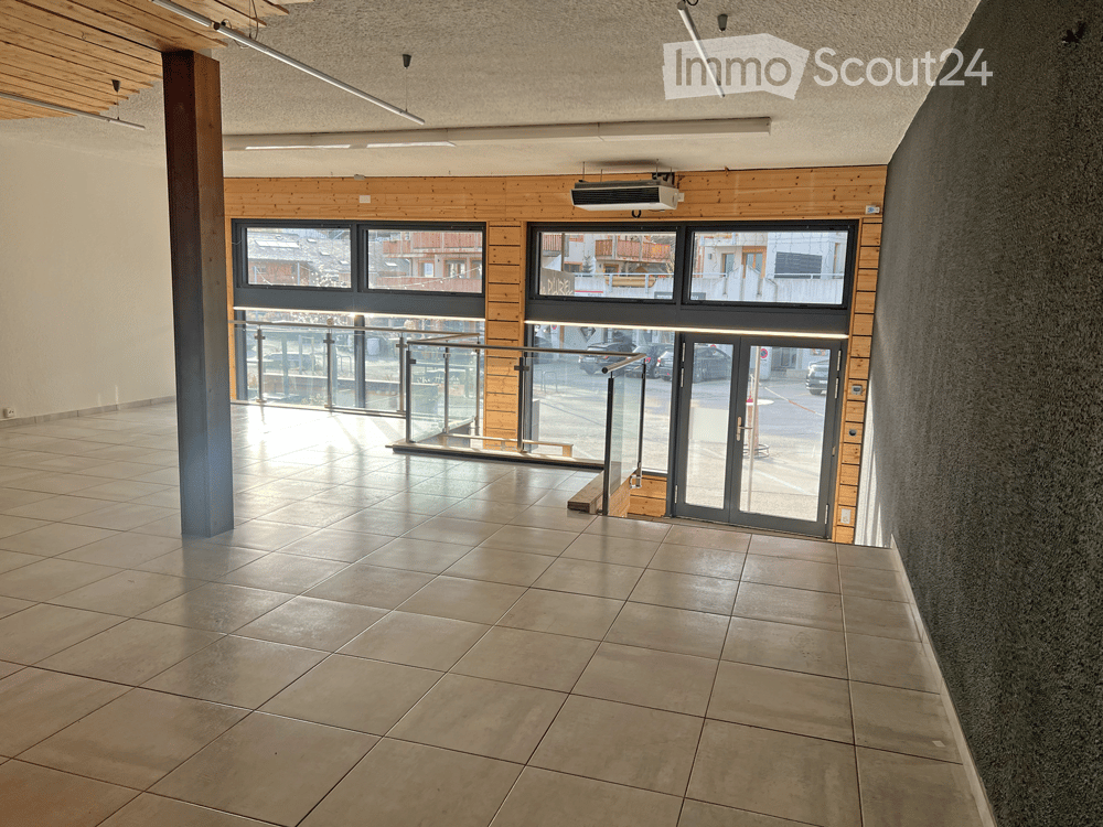 Empty hallway with tiled floor, wooden paneling, large windows, and a glass door leading to an outdoor area.