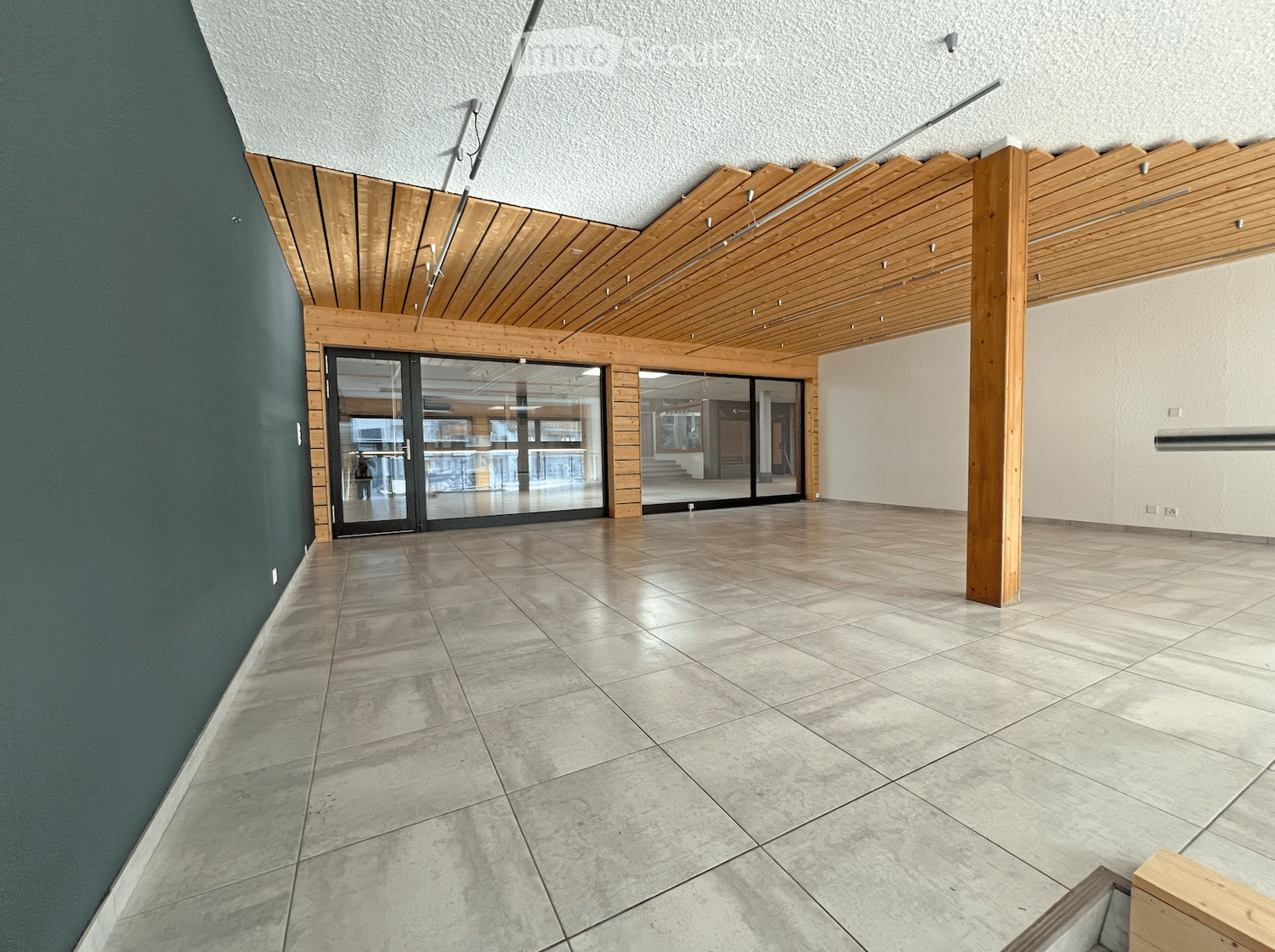 Modern hallway with polished tile flooring, wooden ceiling beams, and large glass doors leading to another area.