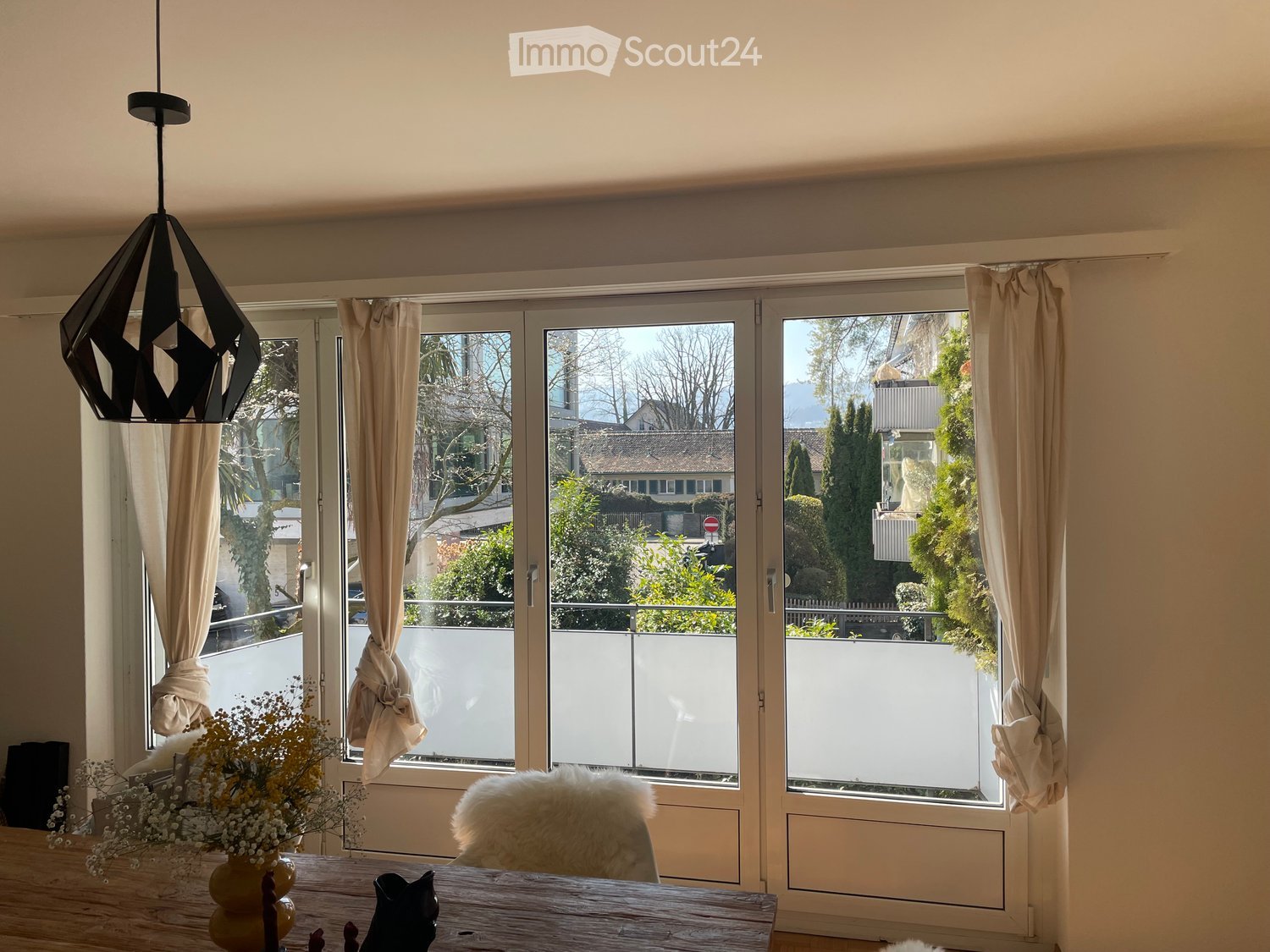 dining room with large windows, wooden table, white chair, flowers, balcony