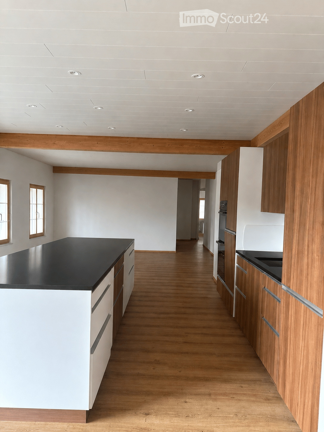 Empty kitchen with white walls, wooden flooring, and modern cabinetry. No furniture or appliances are present.