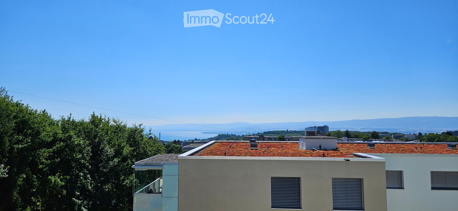 Modern building with a green roof, overlooking a scenic view of a body of water and distant mountains.