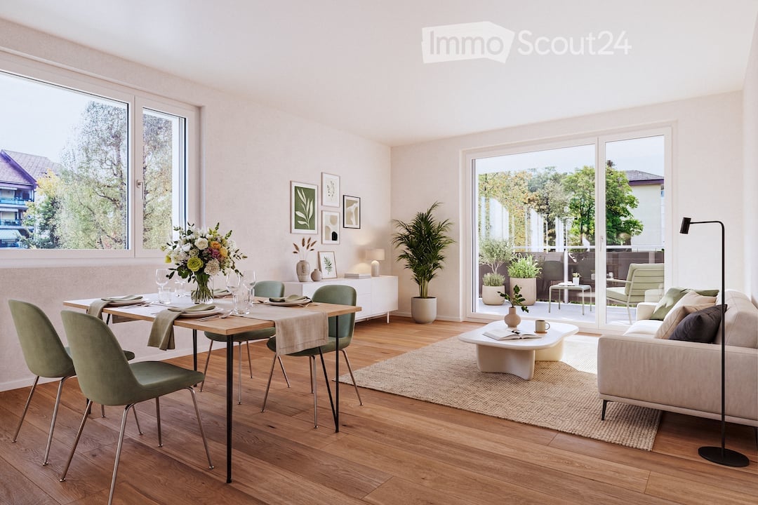 Bright, open living and dining area with wooden flooring, large windows, and a view of greenery. Features a cream sofa, coffee table, dining table with chairs, and decorative vases.