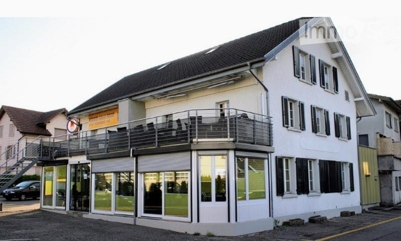 Two-story building with a balcony on the first floor, large windows, and a covered entrance area.