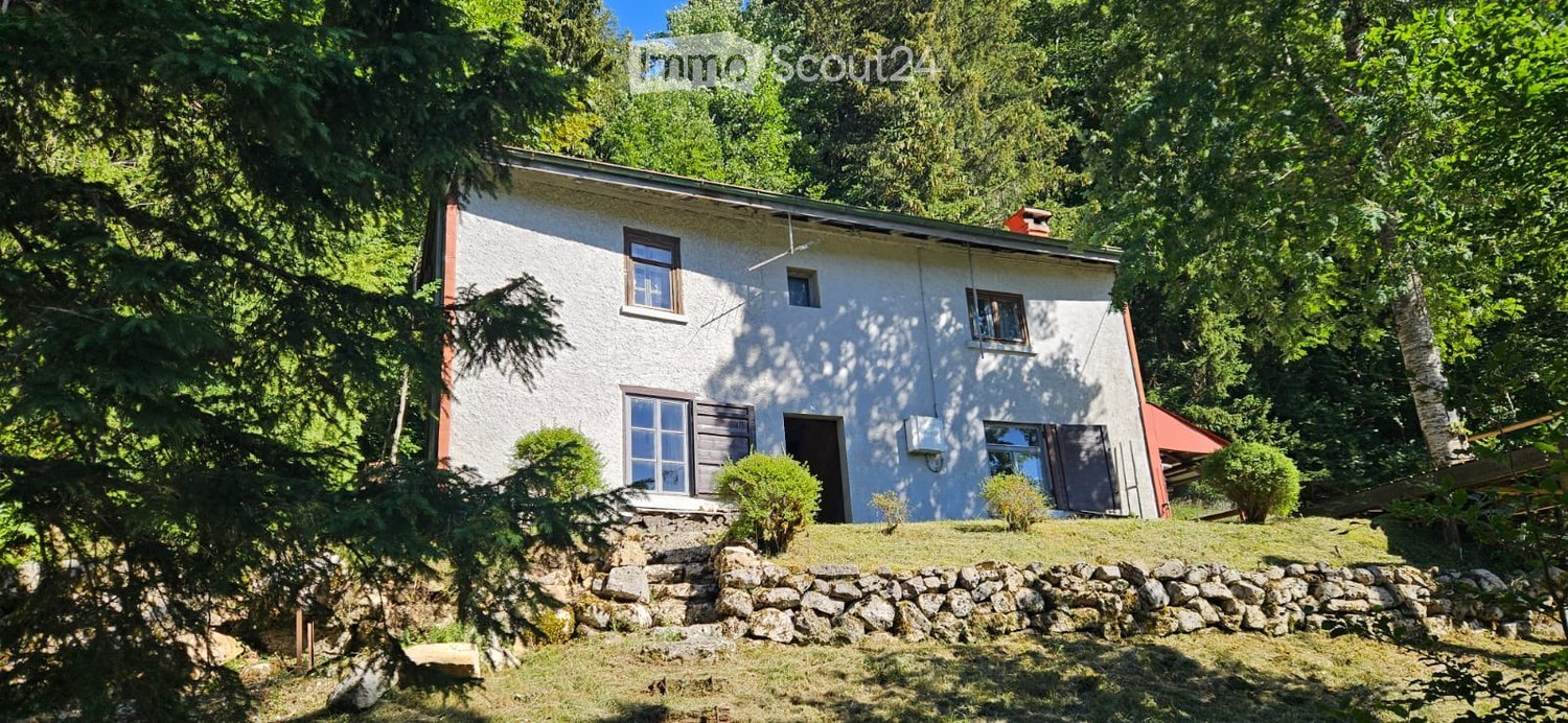 Single-story house with white exterior, multiple windows, and a stone retaining wall in front.