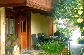 Balcony area with a small table and chairs, surrounded by greenery and potted plants.