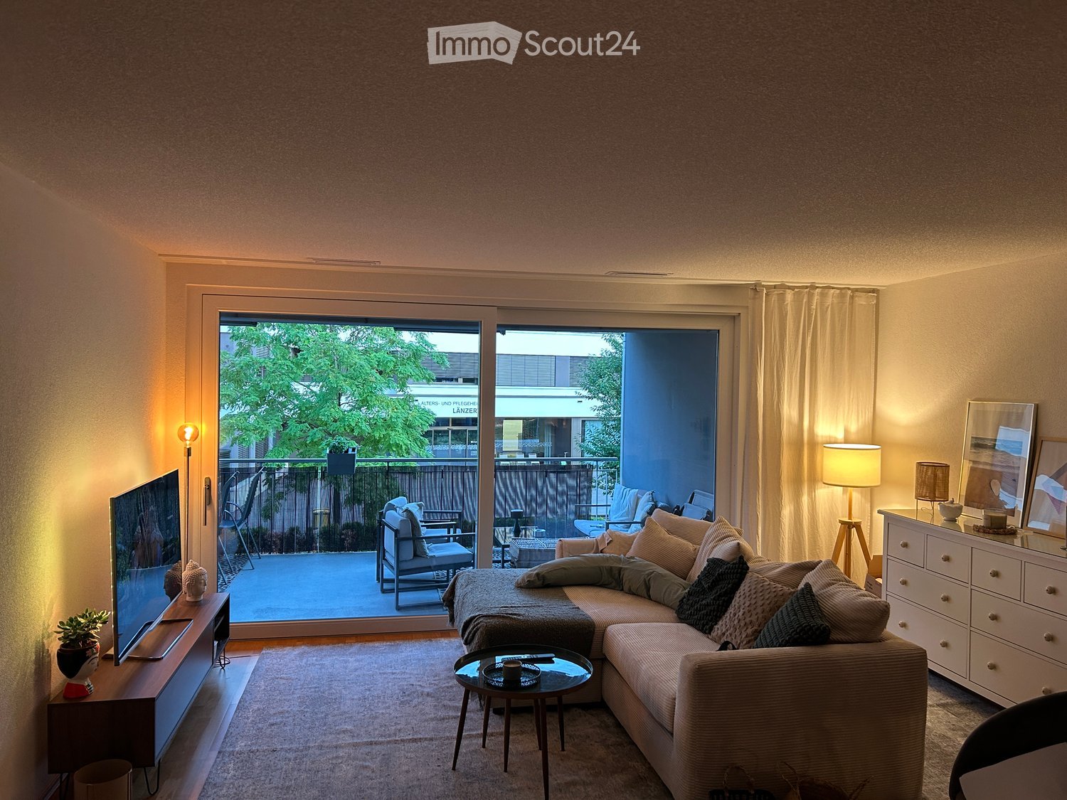 Modern living room with a sectional sofa, coffee table, TV, side table, and balcony access.
