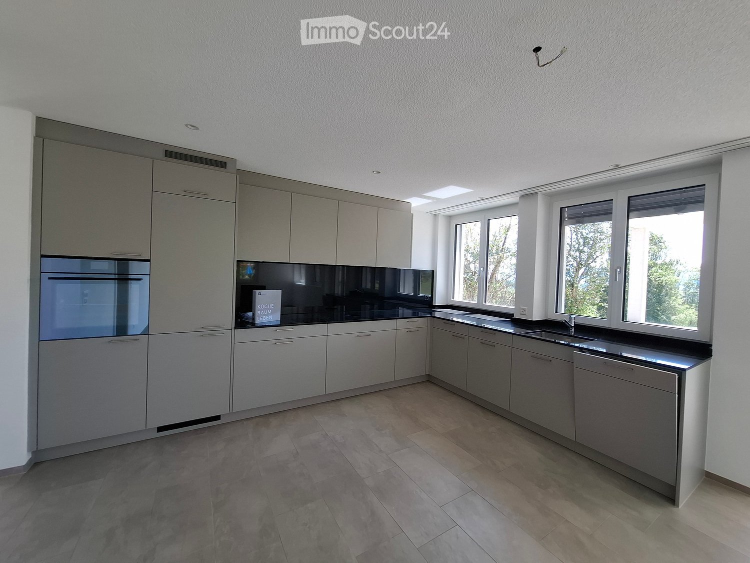 Modern kitchen with grey cabinetry, black countertops, and large windows. Features an oven, sink, and faucet.
