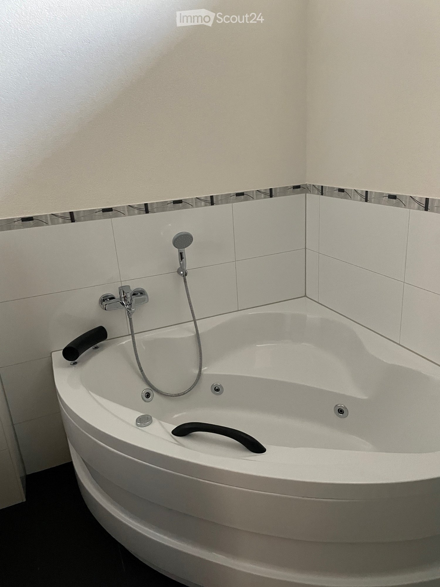 Modern corner bathtub with integrated showerhead and controls, sleek design, white tiles, and a dark floor.