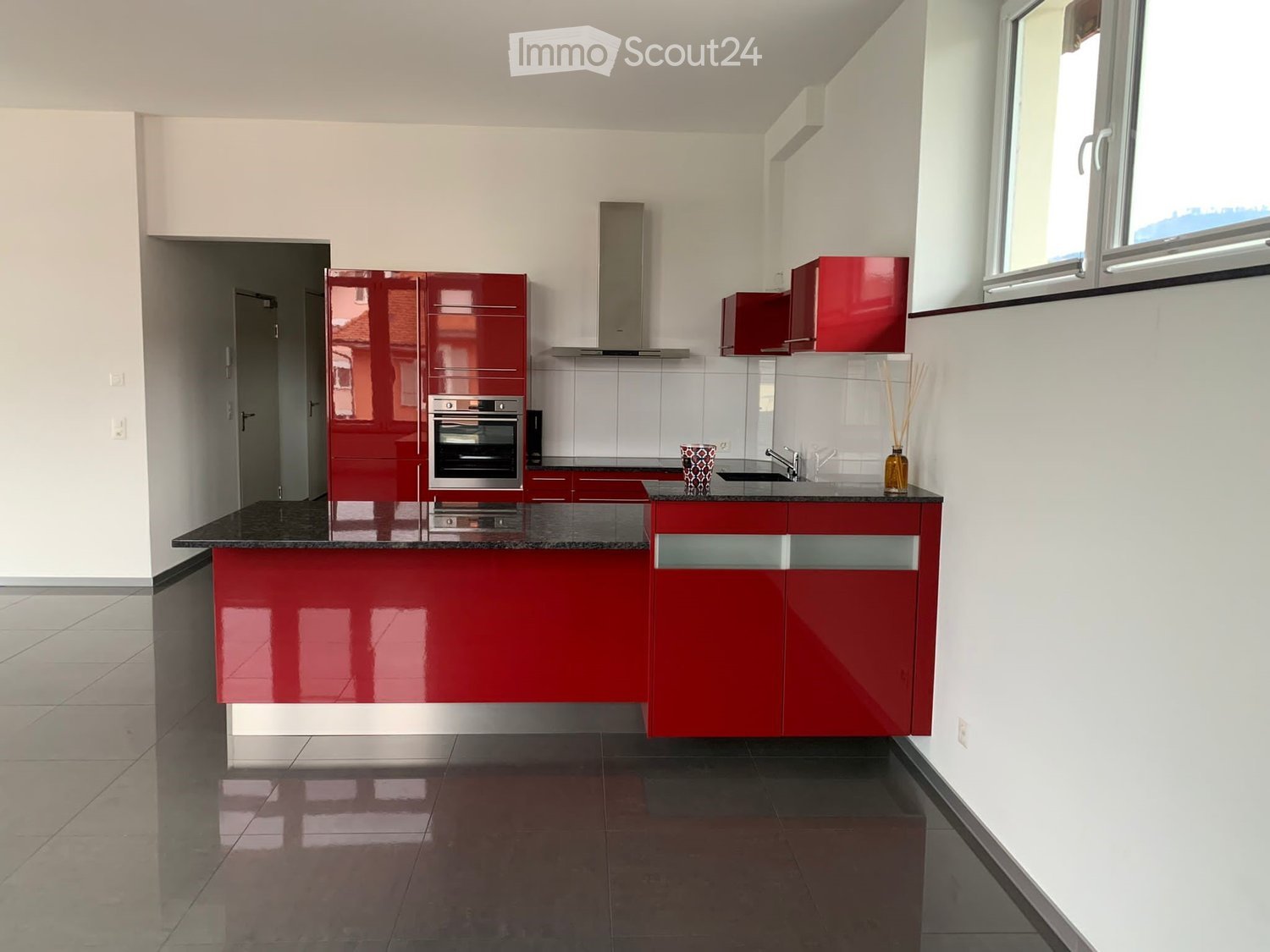 Modern kitchen with red cabinets, stainless steel oven, granite countertop, and large windows.