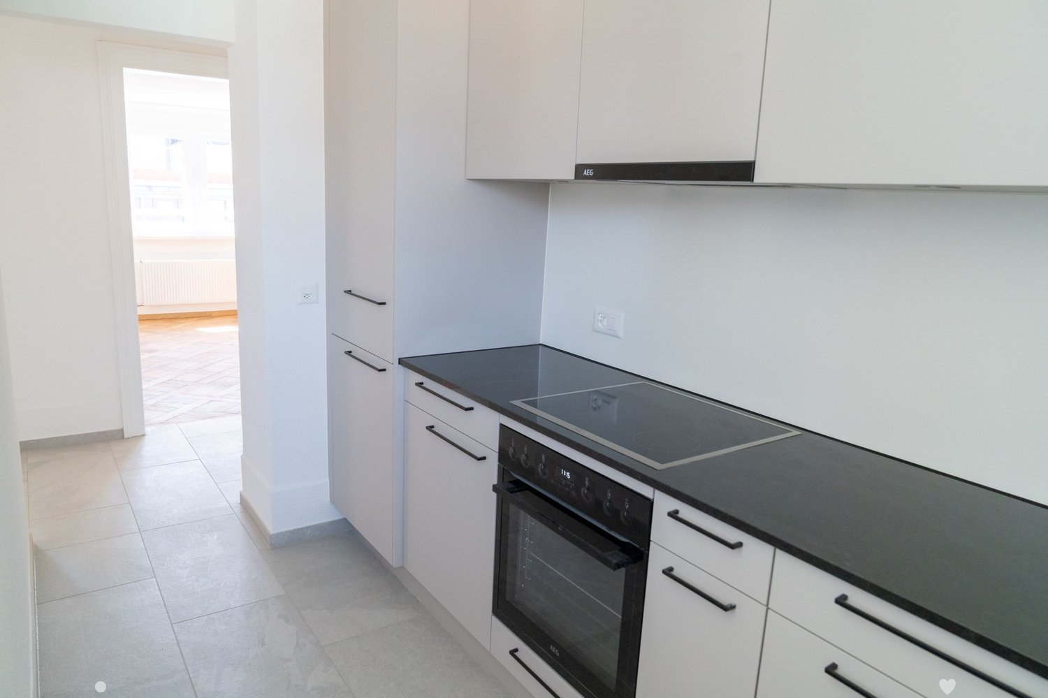 Modern kitchen, white cabinetry, black countertops, built-in oven, tile flooring