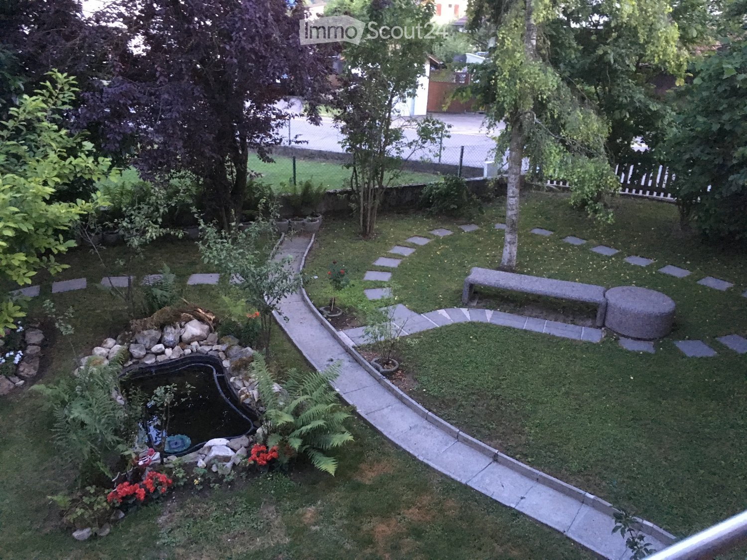 Well-maintained garden with a small pond, stone pathway, benches, and various plants and trees.