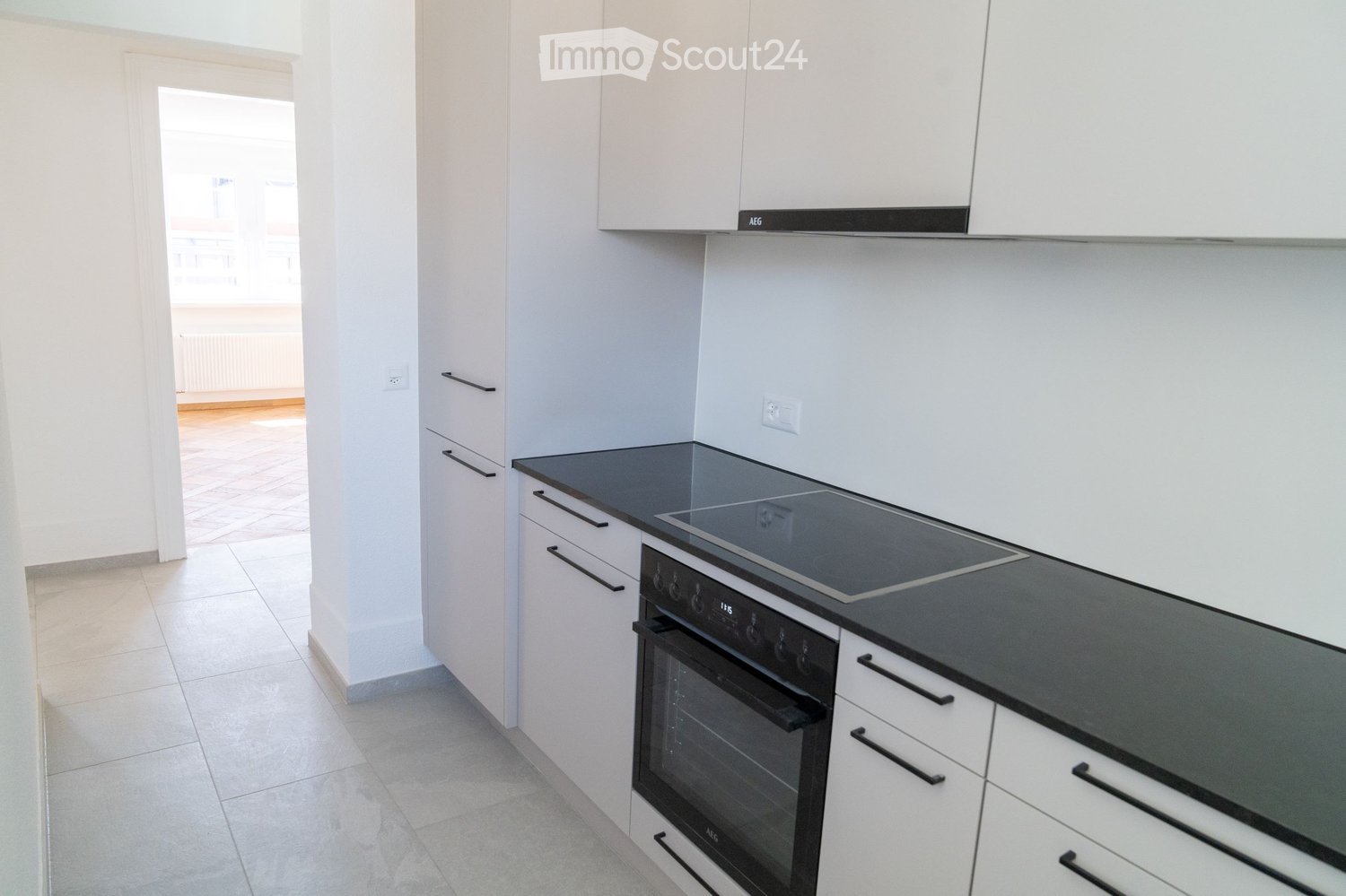 Modern kitchen with white cabinets, black countertops, an induction stove, and an oven. The space is bright and clean with tiled flooring.