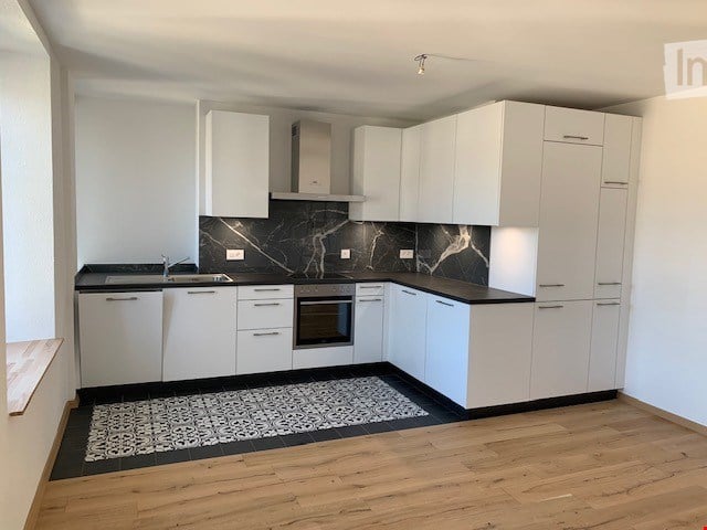 Modern kitchen with white cabinets, black marble backsplash, and wooden flooring. Features a sink, oven, and a decorative rug.