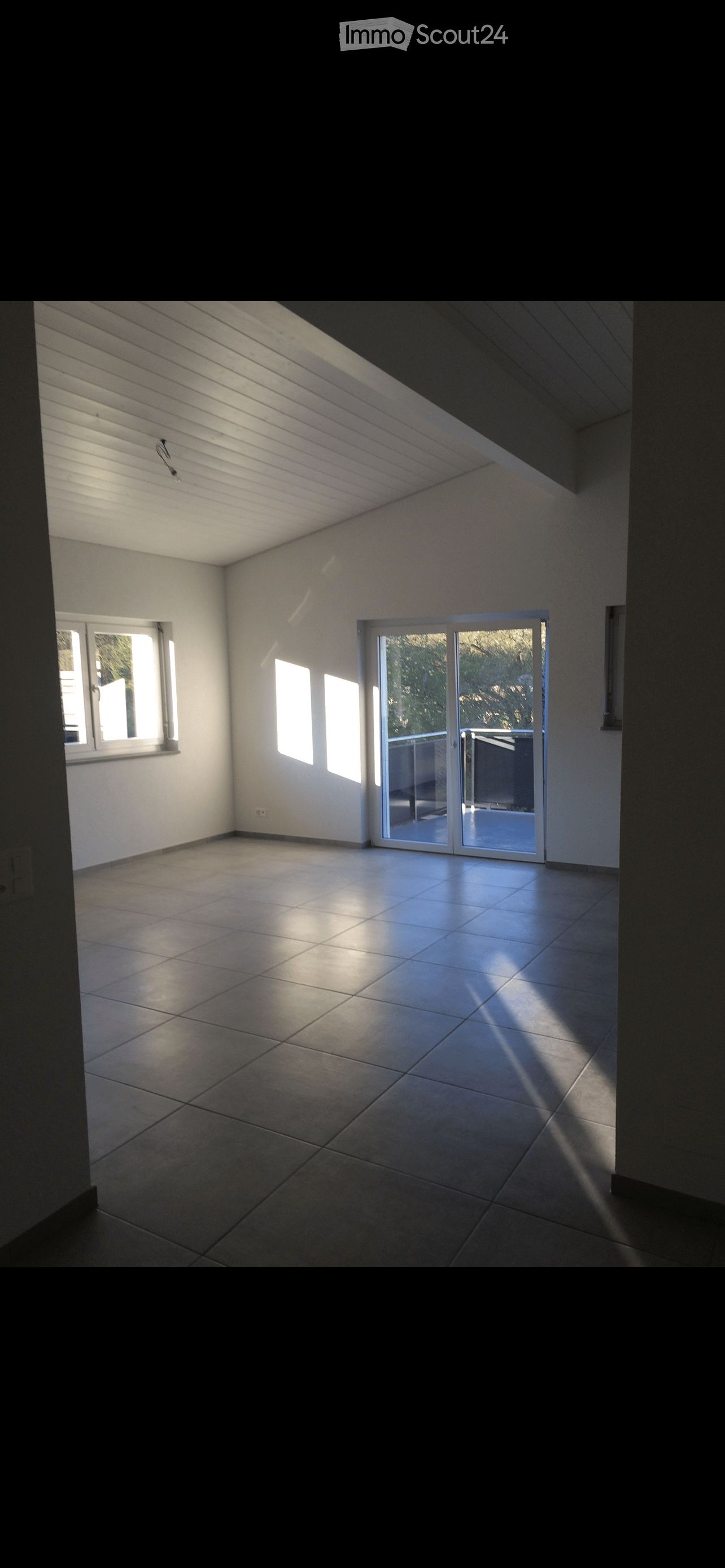 Empty room with tiled floor, white walls, large windows, and a sliding glass door leading to an outdoor area.