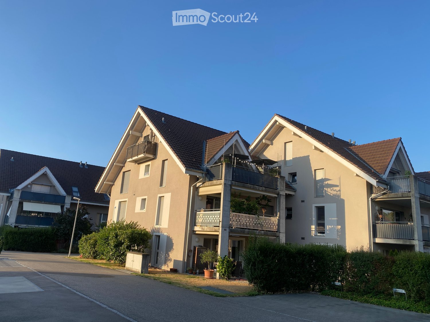 Modern two-story residential building with beige facade, multiple balconies, and a well-maintained garden area.