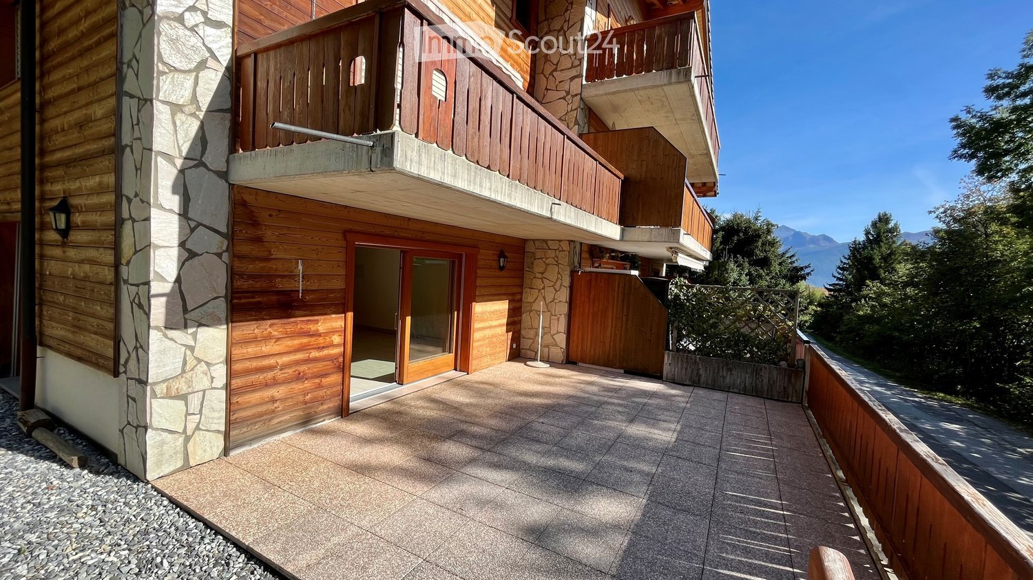 Balcony with wooden railings, stone and wood exterior walls, tiled floor, and scenic mountain view.