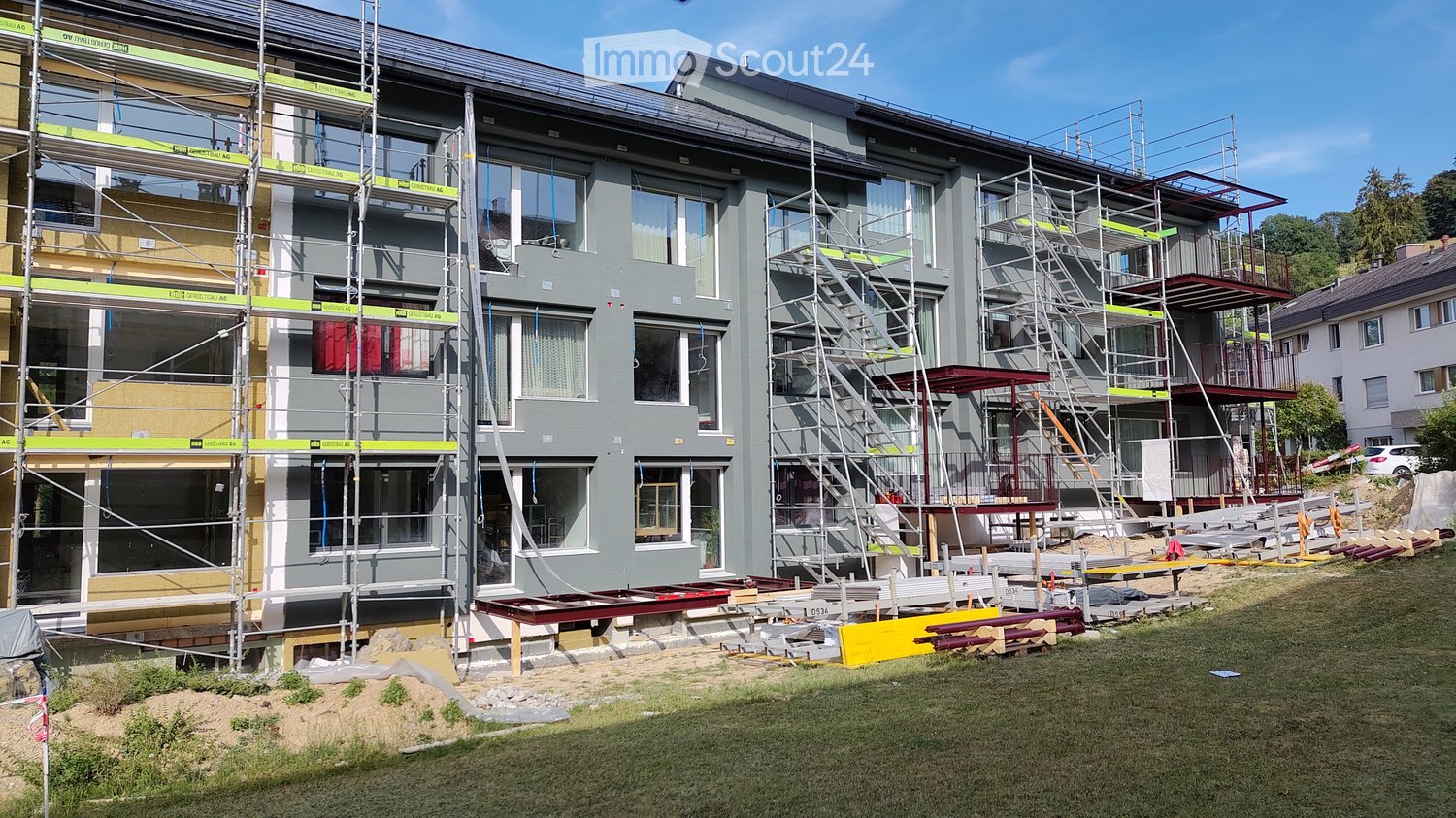 Multi-story residential building under construction with scaffolding, exposed windows, and construction materials on the ground.
