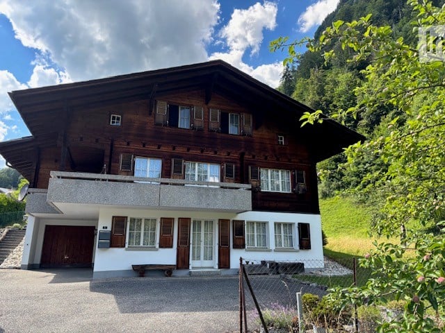 Traditional wooden chalet with multiple windows, garage, and scenic mountain view.