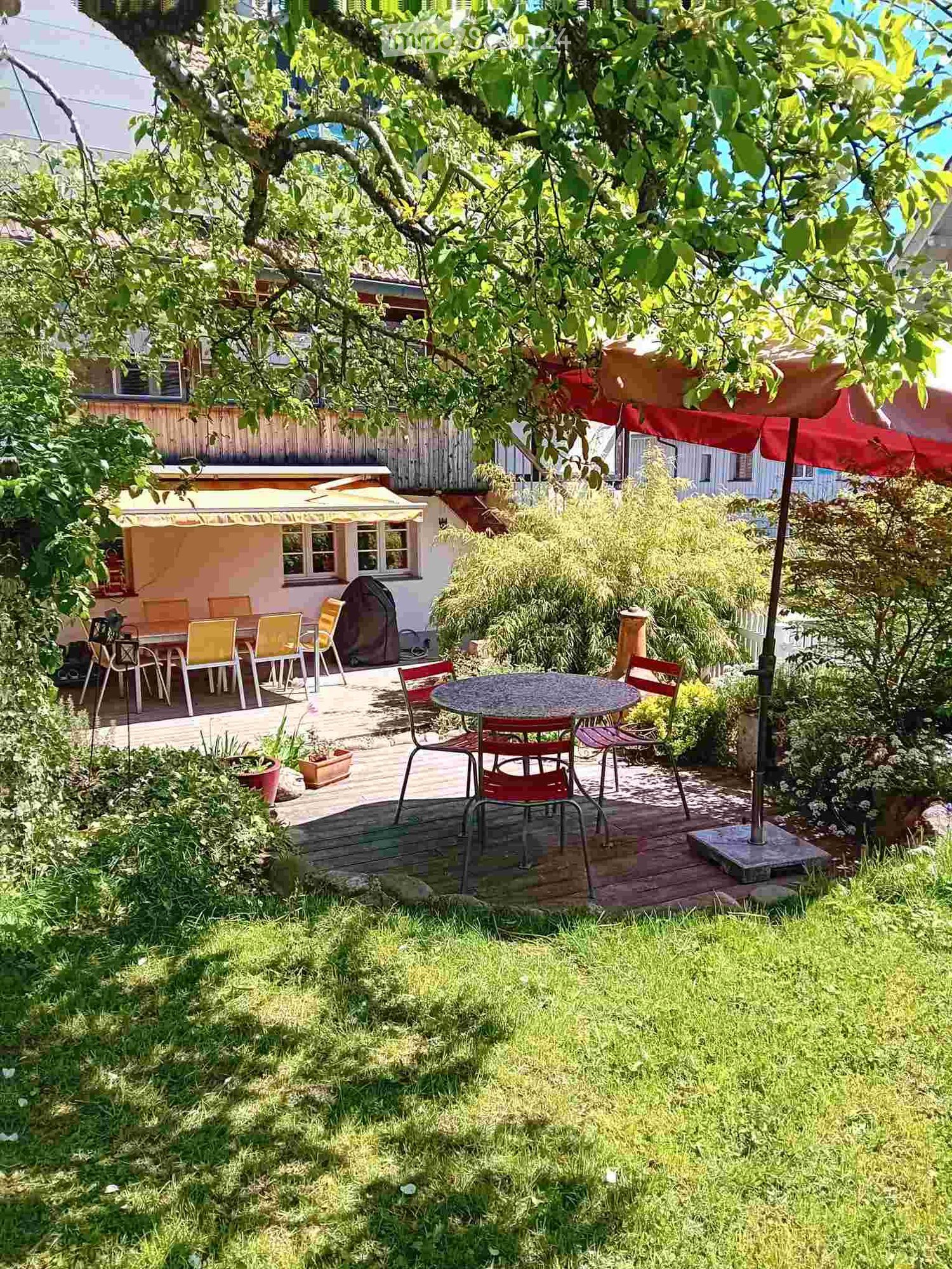 Garden with wooden deck, outdoor dining area, patio furniture, and surrounding greenery.