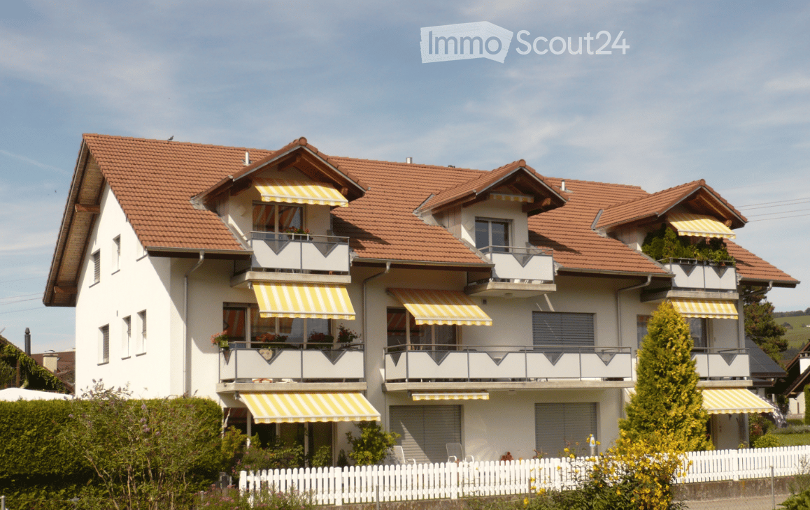 Two-story house with red-tiled roof, white exterior, multiple balconies with striped awnings, and a white picket fence in front.