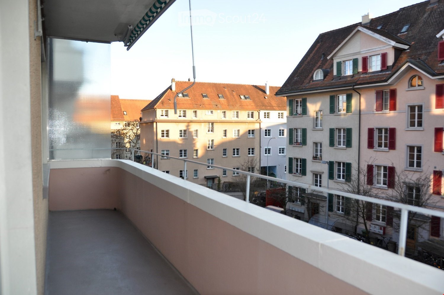 Balcony with a view of a residential area featuring multi-story buildings with red-tiled roofs and green shutters.