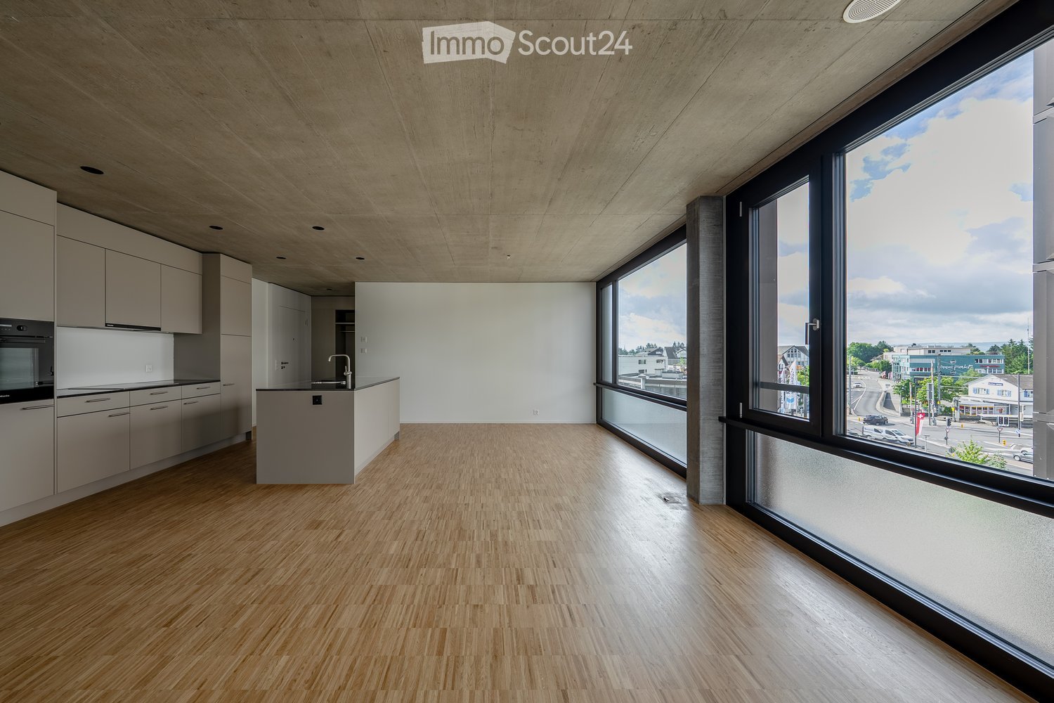 Modern kitchen with light wood flooring, white cabinets, and a large window overlooking a street scene.