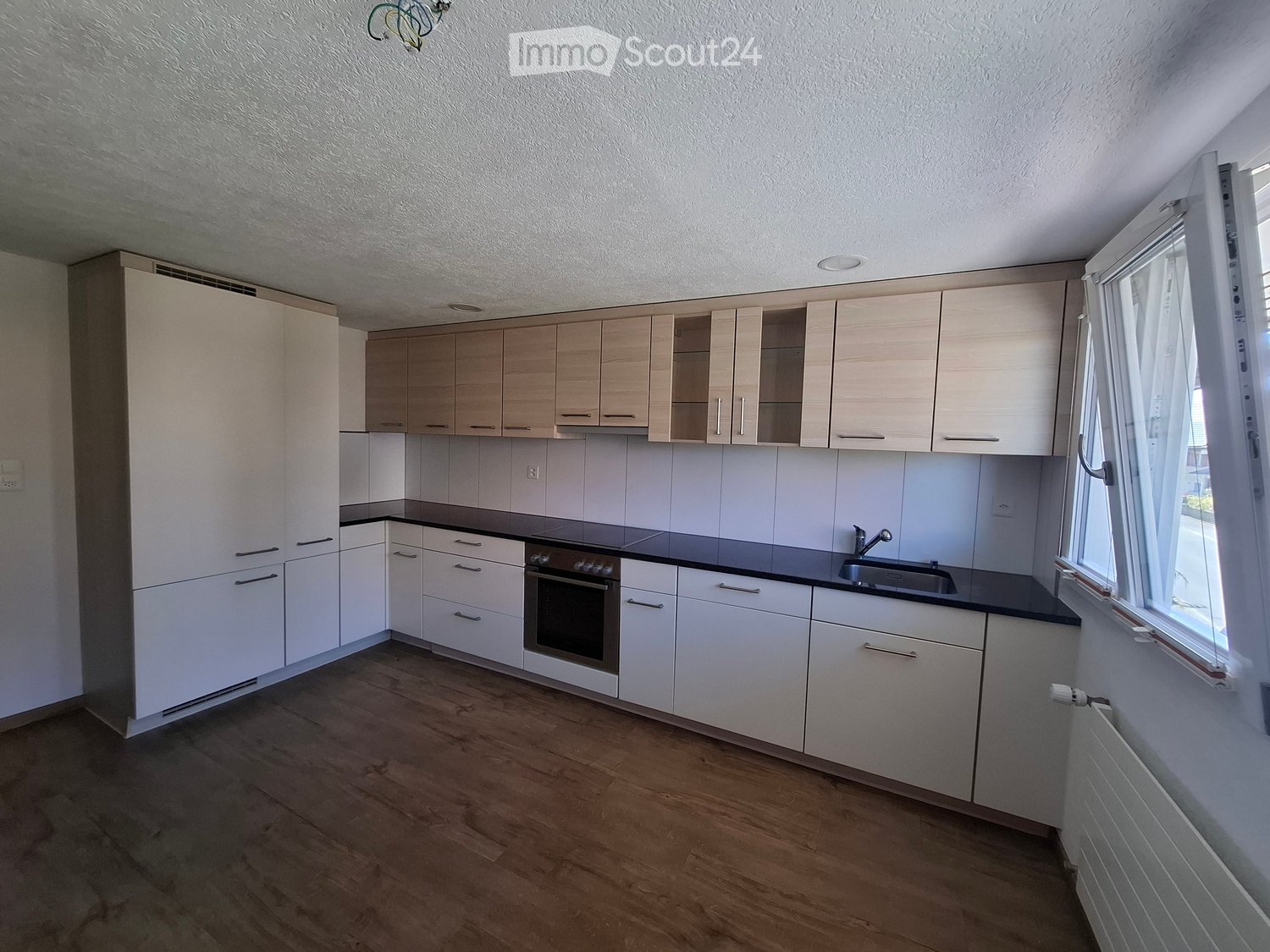Modern kitchen with light wood cabinets, white tiles, and a black countertop. Features an oven, sink, and ample storage space.