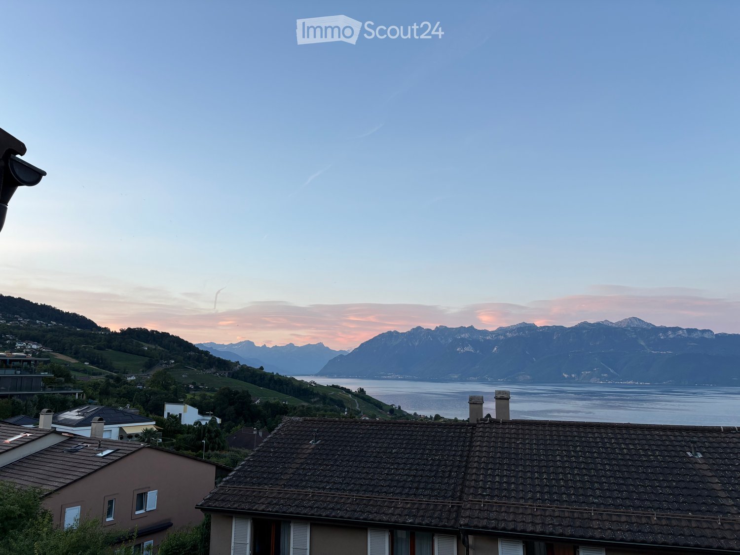 View of rooftops with surrounding landscape, mountains, and lake in the background.