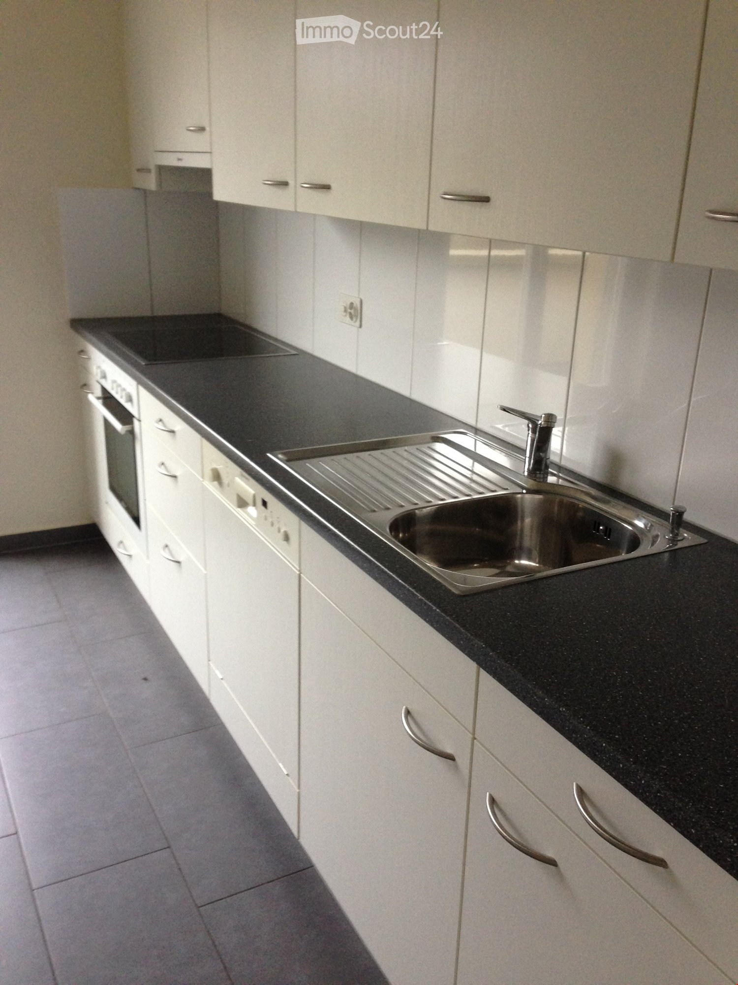 Modern kitchen with white cabinets, black countertop, stainless steel sink, and built-in oven.