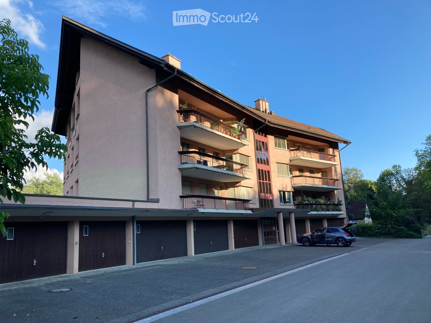 Multi-story residential building with balconies, garage, and parking area.