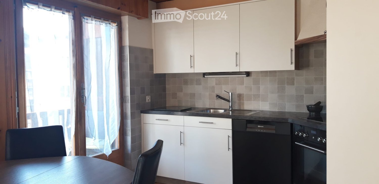 Modern kitchen with white cabinets, black countertops, a sink, dishwasher, oven, and a small dining area with a table and chairs.