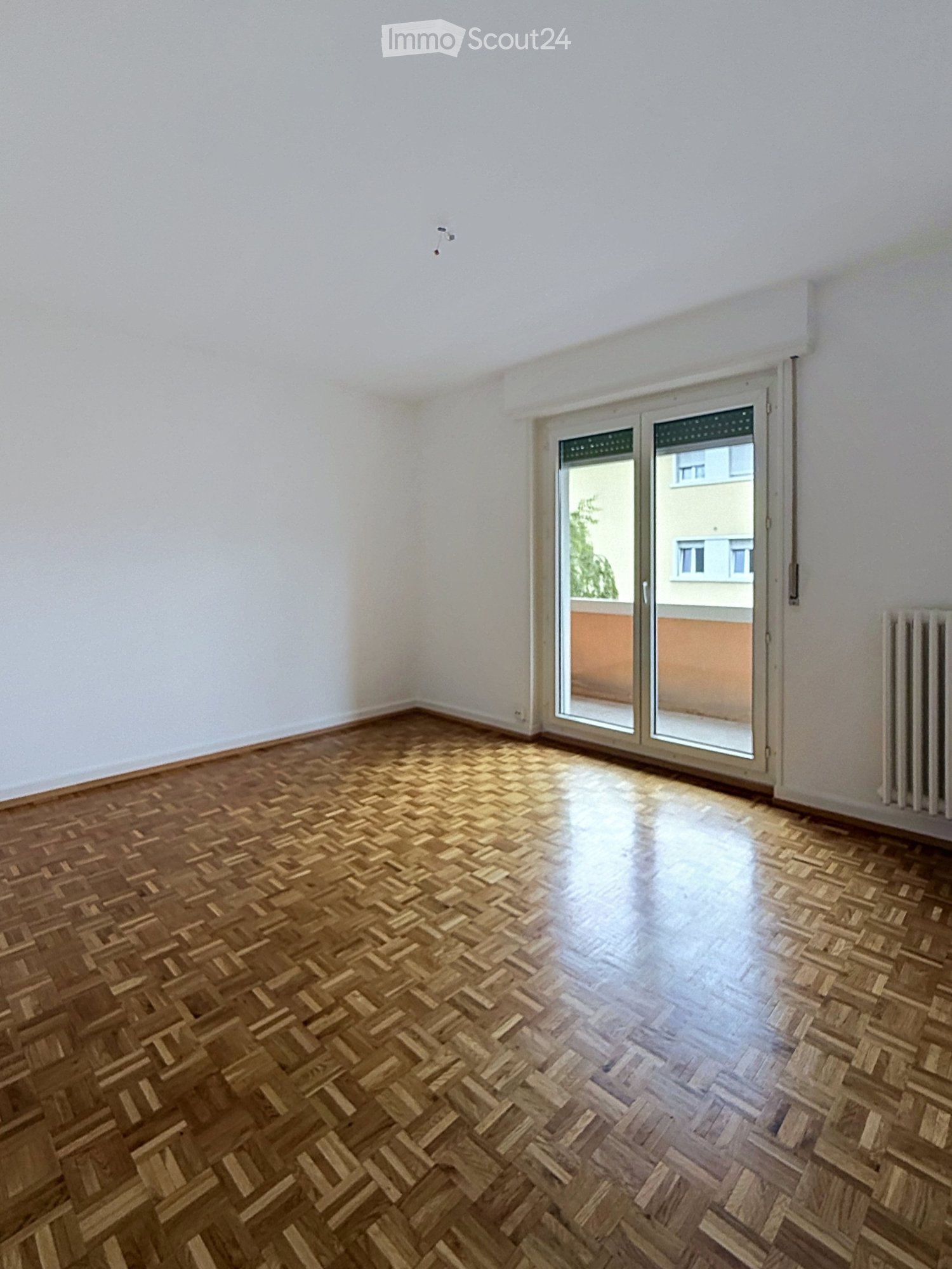 Empty room with wooden herringbone flooring, white walls, and a large sliding glass door leading to a balcony.