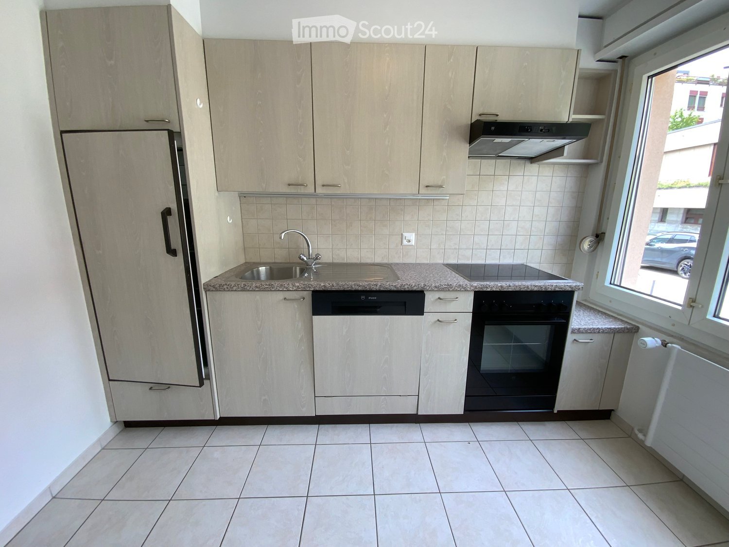 Modern kitchen with light wood cabinets, stainless steel appliances, granite countertop, and tiled floor.