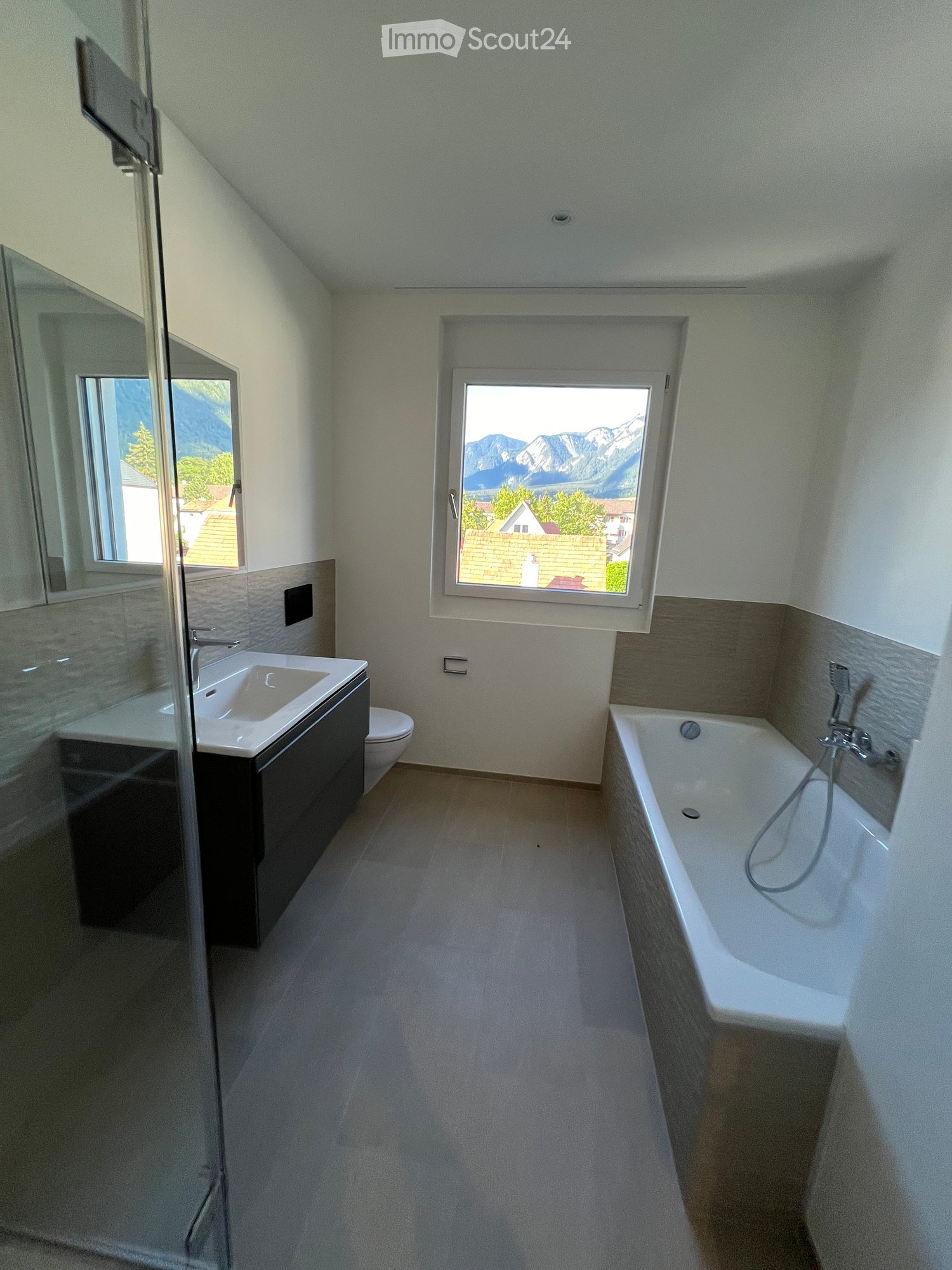 Modern bathroom with a bathtub, sink, toilet, and large windows offering a scenic mountain view.