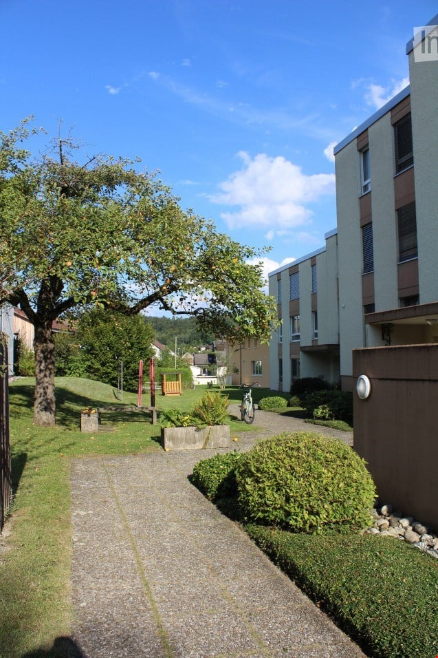 Well-maintained garden area with a tree, pathway, and modern apartment building in the background.