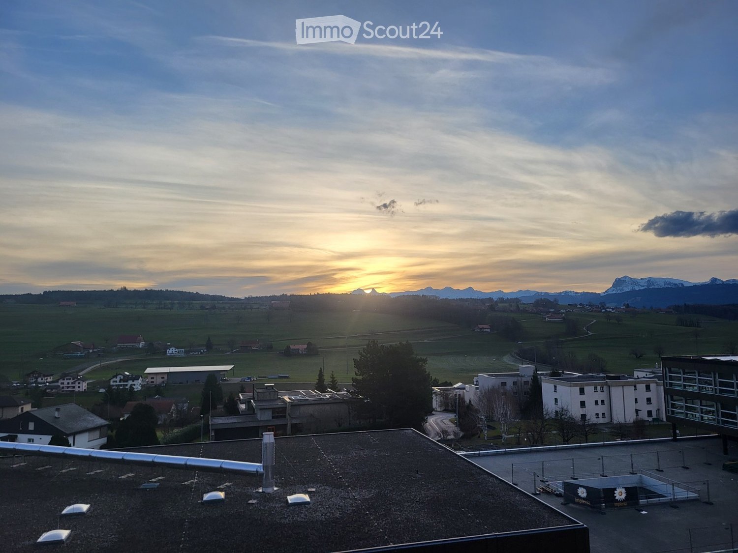 Roof view of a building with surrounding landscape, distant mountains, and sunset sky.