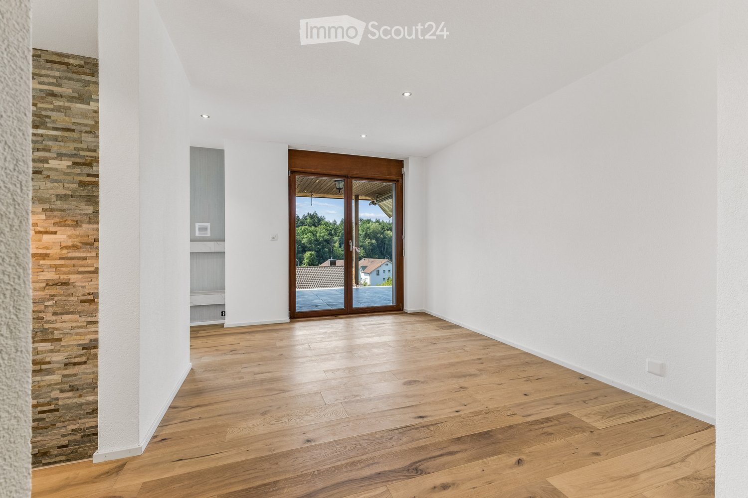Empty room with light wooden flooring, white walls, and a large sliding glass door leading to a balcony or outdoor area.